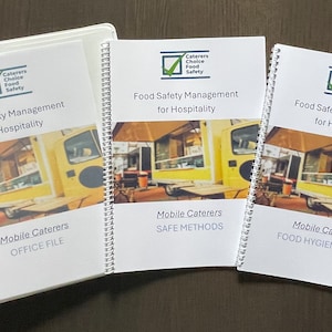 May include: A white binder and two spiral-bound booklets titled Food Safety Management for Hospitality. Each cover features a logo with a green checkmark and an image of a yellow food truck. The booklets are labeled Mobile Caterers Office File, Safe Methods, and Food Hygiene Diary.