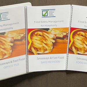 May include: A white binder and two spiral-bound booklets titled Food Safety Management for Hospitality, Takeaways & Fast Food. The covers feature a Caterers Choice Food Safety logo and a graphic of french fries and a burger on a wooden surface.