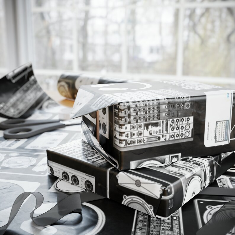 May include: Two black and white gift boxes wrapped in patterned paper with a black and white design. The boxes are stacked on top of each other and are sitting on a table covered in wrapping paper.