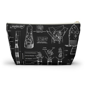 May include: Black wash bag with a white blueprint design of a spacecraft, including the command module, service module, and lunar module. The bag has a gold zip and is suitable for storing toiletries.