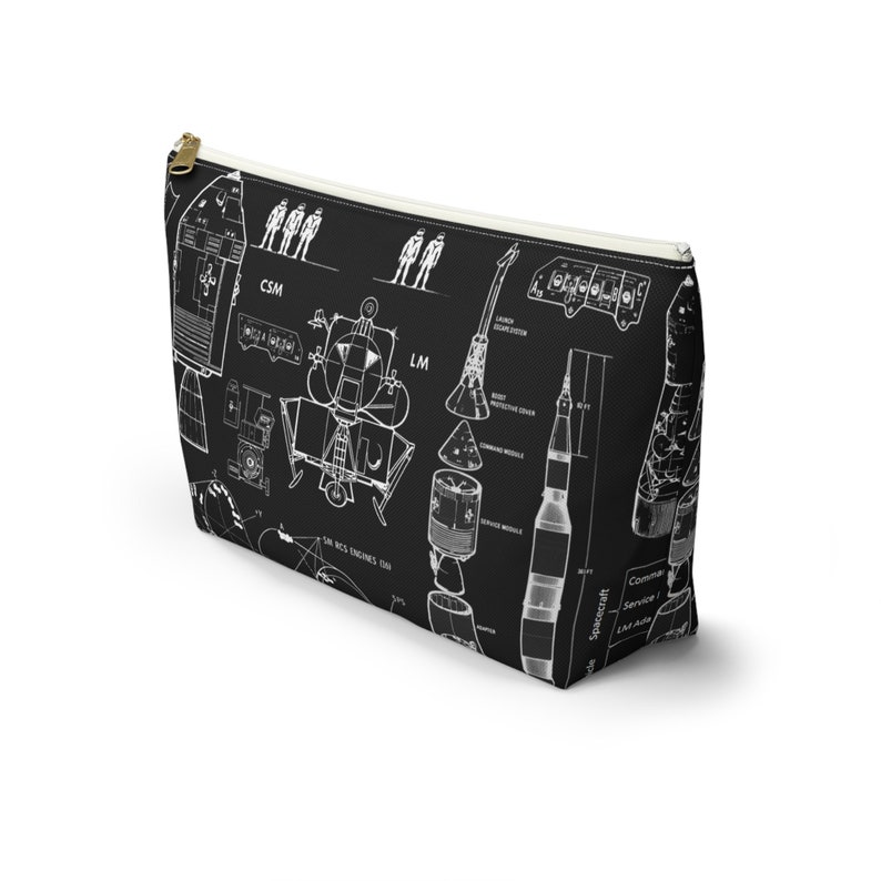 May include: Black cosmetic bag featuring a white diagram of a spacecraft, including the CSM, LM, and rocket components. The bag has a gold zip and a white interior lining. Text includes "SM RCS ENGINES THU" and "Spacecraft".