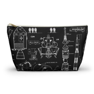 May include: Black cosmetic bag with a white schematic of a spacecraft, including CSM, LM, and rocket parts. The bag has a gold zip and a rectangular shape, ideal for storing makeup or toiletries.