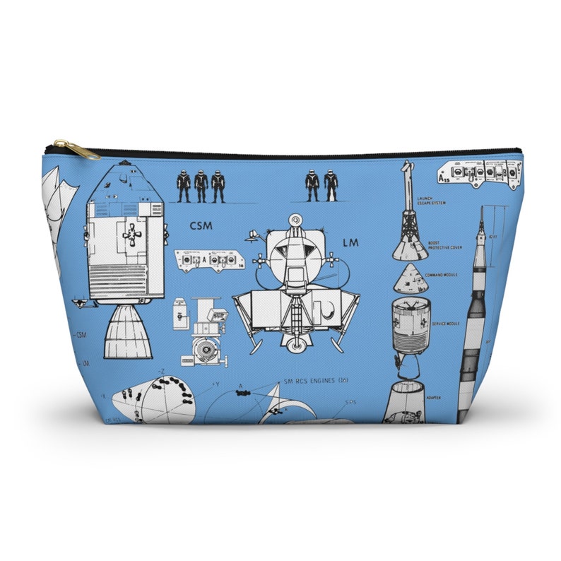 May include: A light blue zipped cosmetic bag with a detailed blueprint design of a spacecraft. The bag has a gold zip and a black trim. The design includes the letters "CSM" and "LM".