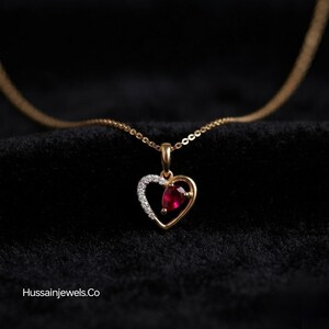 May include: A gold necklace featuring a heart-shaped pendant. One side of the heart is encrusted with small white stones, while the other side holds a single pear-shaped red gemstone. The text Hussainjewels.co is visible in the bottom left corner.