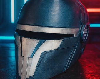 May include: A dark blue helmet with silver accents, featuring a visor and side details. The helmet is displayed against a backdrop of neon blue and red lights, creating a futuristic aesthetic. The design suggests a sci-fi or cosplay theme.