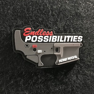 May include: A gray and black patch with the words "Endless Possibilities" in red and white. The patch has a detailed design of a firearm component and the text "Patriot Patch Co."