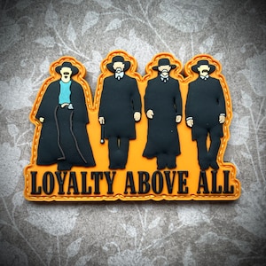 May include: Orange and black embroidered patch with four figures in black suits and hats. The text "LOYALTY ABOVE ALL" is below the figures.