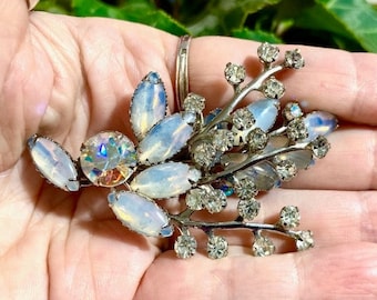 Peut inclure: Une broche argentée avec un groupe de pierres blanches irisées et de strass clairs dans un motif floral.