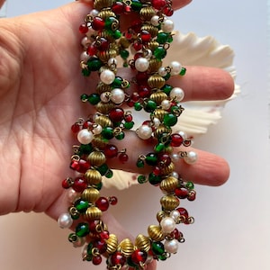 Peut inclure: Un collier festif composé de perles rouges, vertes et blanches, entrecoupées d'éléments métalliques dorés. Les perles sont regroupées, créant un design texturé et accrocheur. Le collier est probablement destiné à des occasions spéciales.