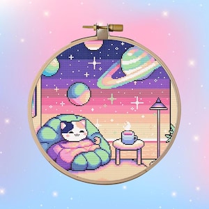 May include: A cross-stitch pattern depicting a cat relaxing in a green armchair with a cup of coffee on a table. The background shows a colourful galaxy with stars and planets.