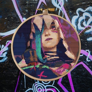 May include: A cross-stitch embroidery hoop with a colorful portrait of a woman with green and purple hair. The woman is wearing a black and white outfit with a pink and green design.