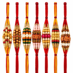 May include: Seven decorative wrist bands featuring red and yellow thread strands adorned with various beads, including metallic gold cylinders, white pearls, green, orange, and red spheres, and carved floral-shaped accents in a vertical arrangement.