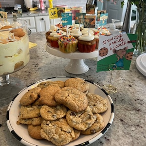 Op de afbeelding: Een tafeldekking voor een kinderfeestje met verschillende lekkernijen, waaronder een trifle, cupcakes en chocoladekoekjes. De tafel is versierd met boekenthemadecoraties, waaronder een bord met de tekst "Als je een muis een koekje geeft".