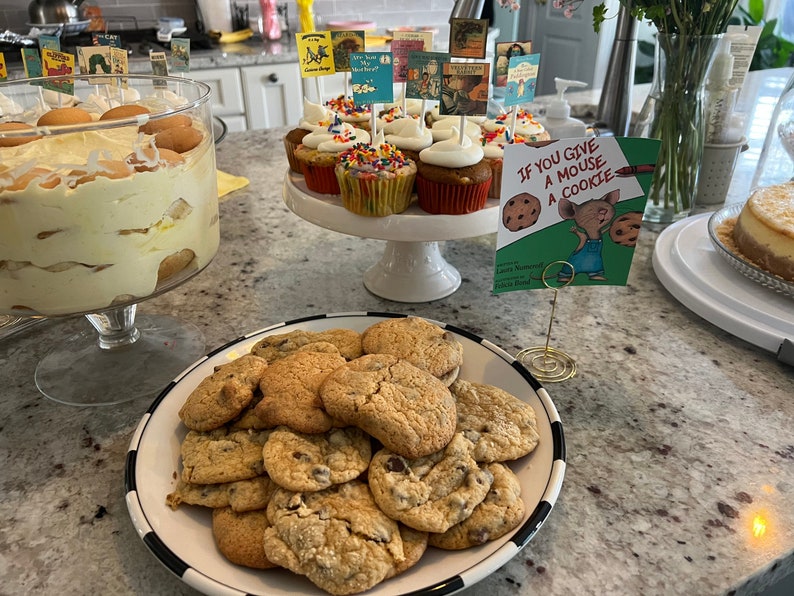 Op de afbeelding: Een tafeldekking voor een kinderfeestje met verschillende lekkernijen, waaronder een trifle, cupcakes en chocoladekoekjes. De tafel is versierd met boekenthemadecoraties, waaronder een bord met de tekst "Als je een muis een koekje geeft".