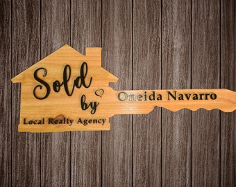 May include: A wooden key-shaped sign with the words "Sold by Local Realty Agency" and "Oneida Navarro" on it.