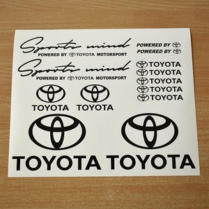 Op de afbeelding: Een set zwarte en witte vinyl stickers met de woorden "Sports mind" en het Toyota logo. De stickers zijn ontworpen om op een auto of ander oppervlak te worden aangebracht.
