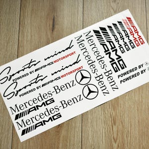 Puede incluir: Una hoja blanca de pegatinas con texto negro y rojo. Las pegatinas presentan las palabras "Sports mind", "Powered by AMG Motorsport", "Mercedes-Benz", "AMG" y "Powered by".