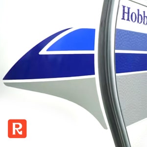May include: A white camper with blue and gray stripes and the word "Hobby" on the side. The camper has a white, blue, and black graphic on the front.