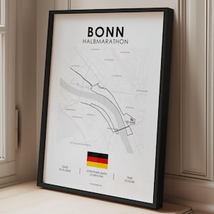 Könnte beinhalten: Gerahmter Druck der Streckenkarte des Bonn Halbmarathons. Die Schwarz-Weiß-Karte zeigt die Rennstrecke mit der deutschen Flagge und Veranstaltungsdetails unten. Der Rahmen ist schwarz.