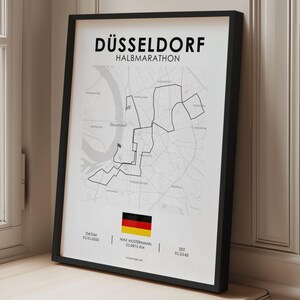 Könnte beinhalten: Schwarz gerahmter Druck mit dem Text "DÜSSELDORF HALBMARATHON" und einer Karte von Düsseldorf. Die deutsche Flagge ist unten mit den Renndetails: Datum, Name des Läufers, Distanz (21,0975 km) und Zeit.