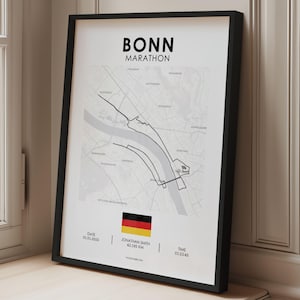 Könnte beinhalten: Gerahmter Druck der Bonn Marathon Karte, mit der Rennstrecke in schwarzen Linien auf hellgrauem Hintergrund. Die deutsche Flagge ist unten abgebildet, mit dem Text "BONN MARATHON" oben. Der Rahmen ist schwarz.