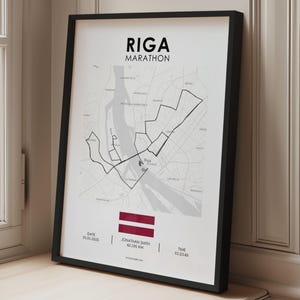Könnte beinhalten: Gerahmter Druck des Streckenplans des Riga-Marathons. Die Schwarz-Weiß-Karte zeigt die Strecke, die Straßen der Stadt und die lettische Flagge. Der Text enthält den Namen des Marathons, das Datum, den Namen des Läufers, die Distanz (42,195 km) und die Zeit.