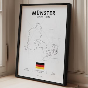 Könnte beinhalten: Ein gerahmter Druck mit der Karte des "Münster Marathon" in Schwarz und Weiß. Der Druck enthält die deutsche Flagge, das Datum, den Namen des Läufers, die Distanz (42,195 km) und die Zeit. Der Rahmen ist schwarz, und der Druck wird auf einer Holzoberfläche präsentiert.