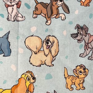 May include: Light blue fabric featuring cartoon illustrations of various dogs and cats. The characters are in different colors, including brown, tan, and orange. The background has a pattern of small, irregularly shaped dots in shades of blue and pink.