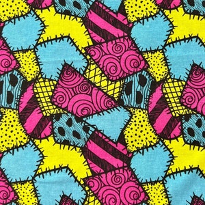 May include: A patchwork fabric with a repeating pattern of blue, yellow, pink, and black shapes. The shapes are sewn together with a zig-zag stitch. The fabric has a textured surface.