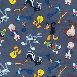 May include: A gray fabric with a repeating pattern of cartoon characters from the Looney Tunes franchise. The characters include Bugs Bunny, Daffy Duck, Tweety Bird, Road Runner, Wile E. Coyote, and Sylvester the Cat.