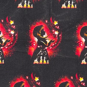 May include: A black fabric with a repeating pattern of a silhouette of a woman with long hair, wearing a dress and blowing on a swirling cloud of red and orange leaves. The woman is surrounded by a glowing halo of light. The pattern also includes a silhouette of a castle and two figures standing in front of it.