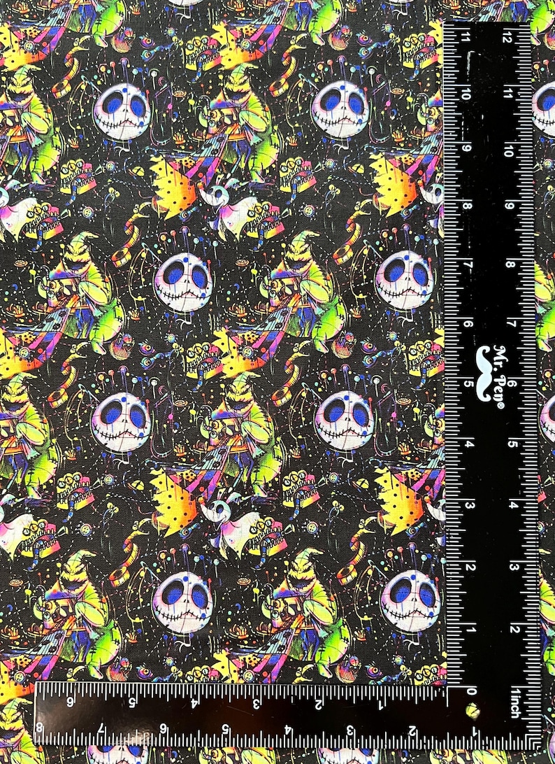 May include: A black fabric with a repeating pattern of a green and purple character with a stitched face, a black and white stitched face, and other colorful details. The fabric is measured with a ruler in inches.