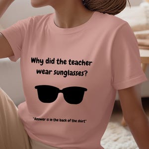 Funny Teacher T-Shirt, "Bright Students" Graphic Tee, Unisex Shirt with Quote: Why did the teacher wear sunglasses? a black sunglasses is designed in the apparel. *Answer is in the back of the shirt - Because her students sere so bright! Female model wearing blossom color t-shirt.