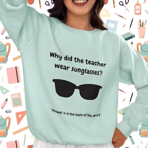 Funny Teacher Sweatshirt, "Bright Students" Graphic Pullover, Unisex Cozy Apparel with Quote: Why did the teacher wear sunglasses? a black sunglasses is designed in the apparel. *Answer is in the back of the shirt - Because her students sere so bright! Female model wearing agave color sweatshirt.