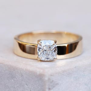 Puede incluir: Un anillo de banda de oro con un diamante de talla cojín.
