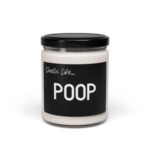 May include: A white candle in a glass jar with a black lid. The label on the jar reads "Smells like... POOP".