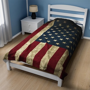 May include: A white twin-sized bed frame with a red, white, and blue American flag patterned comforter. The comforter has a distressed, vintage look.