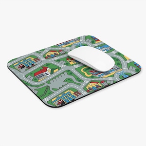 May include: A rectangular mousepad featuring a colorful town map design with roads, buildings, and green spaces. A white wireless mouse rests on the pad. The mousepad has a black border.