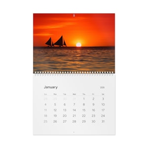 May include: A wall calendar showing a sunset over the sea with sailboats. The calendar displays the month of January 2026. The image shows a bright orange sky and the sun setting over the water.
