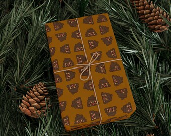 May include: A brown gift box wrapped in paper with a repeating pattern of cartoon poo emojis. The box is tied with twine and is sitting on a bed of green pine needles.