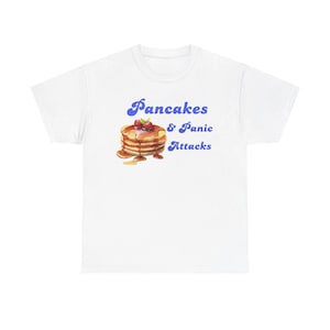May include: White t-shirt with a blue graphic of a stack of pancakes with the text "Pancakes & Panic Attacks"
