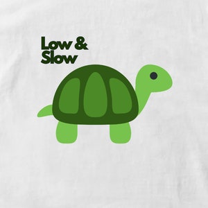 Könnte beinhalten: Ein weißes T-Shirt mit einer grünen Comic-Schildkröte und dem Text "Low & Slow" in Schwarz.