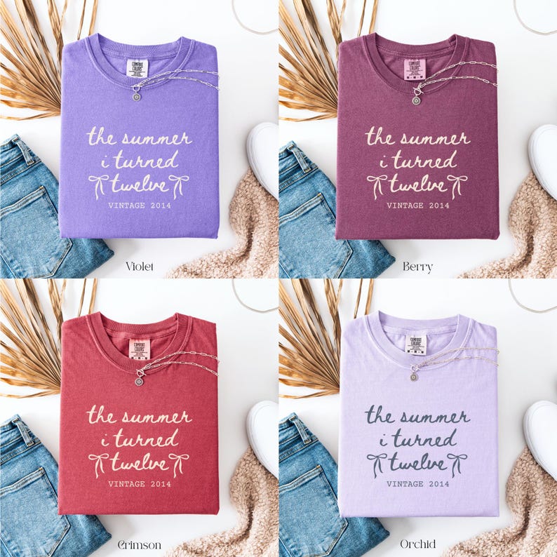 May include: Four t-shirts in violet, berry, crimson, and orchid colors, each folded and displaying the text "the summer i turned twelve VINTAGE 2014". Each shirt has a necklace and is paired with jeans and a neutral-colored scarf.