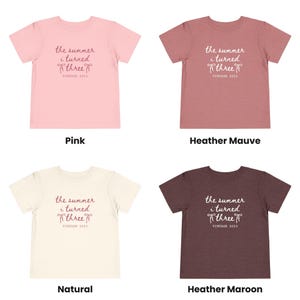 Puede incluir: Cuatro camisetas en rosa, malva jaspeado, natural y granate jaspeado. Cada camiseta tiene el texto "the summer i turned three VINTAGE 2023" en cursiva. Las camisetas se muestran sobre un fondo blanco.