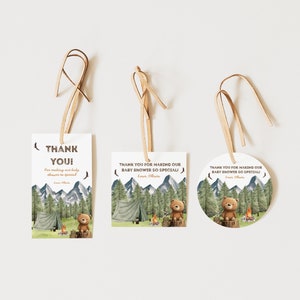 May include: Three thank you tags with a woodland theme. The tags feature a brown bear sitting by a campfire in a forest setting. The text on the tags reads "Thank You!" and "Thank you for making our baby shower so special!"
