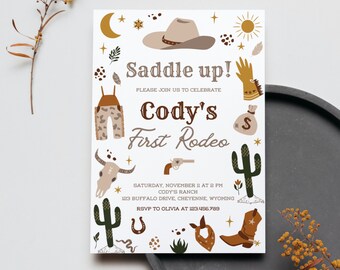 May include: A white invitation with brown, green, and yellow illustrations of a cowboy hat, cactus, boots, and other western-themed imagery. The text reads "Saddle up! Please join us to celebrate Cody's First Rodeo. Saturday, November 11 at 2 PM Cody's Ranch 123 Buffalo Drive, Cheyenne, Wyoming RSVP to Olivia at 123.456.789"