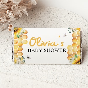 Könnte beinhalten: Weiße Schokoladentafelverpackung mit einem Sonnenblumen-, Waben- und Bienenmuster. Der Text auf der Verpackung lautet "Olivia's Baby Shower".