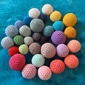 Könnte beinhalten: Eine Sammlung zahlreicher kugelförmiger Häkelbälle in einer Vielzahl von Unifarben, darunter Weiß, Gelb, Orange, Rot, Rosa, Lila, Blau, Grün, Grau, Braun und Schwarz, wobei jeder Ball ein ausgeprägtes, strukturiertes Maschenmuster aufweist.