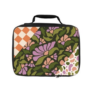 Op de afbeelding: Een zwarte lunchtas met een ritssluiting en een handvat. De tas heeft een patchwork-ontwerp met een bloemenpatroon, een geruit patroon en een gestippeld patroon in tinten groen, roze, oranje en wit.