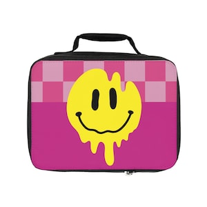 Könnte beinhalten: Rosa Lunchbox mit schwarzem Griff und einem gelben Smiley mit tropfenden Rändern. Der Hintergrund ist ein rosa-weißes Karomuster.